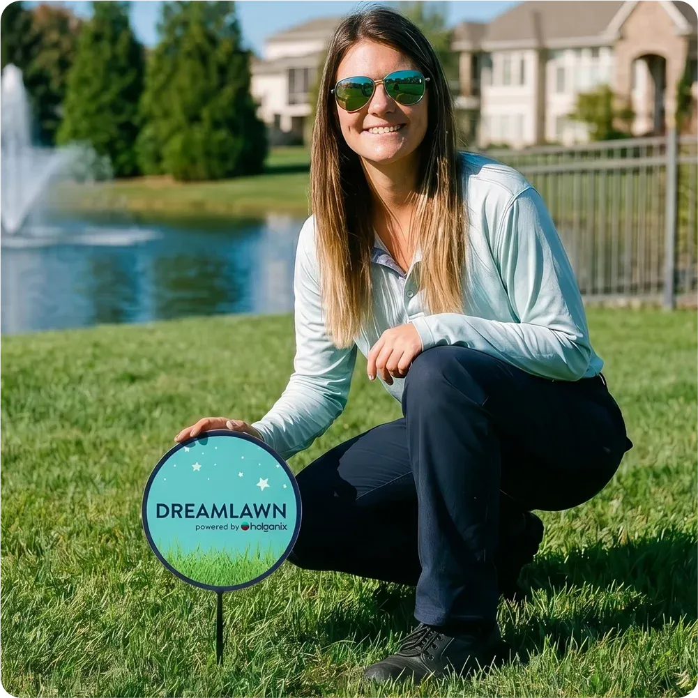 DreamLawn technician kneeling next to DreamLawn lawn sign in a backyard with green healthy grass